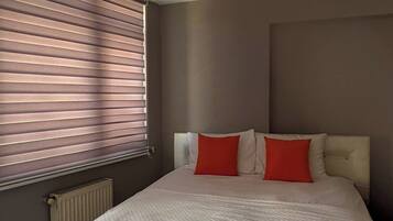 A bedroom with a large bed, a radiator, and a window with blinds.