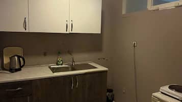 A compact kitchen with a sink, cabinets, a kettle, and a small refrigerator.