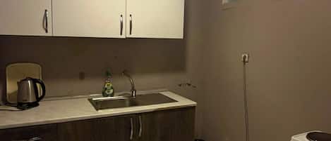 Eine kleine Küche mit Spüle, Schränken, einem Wasserkocher und einem Kühlschrank.