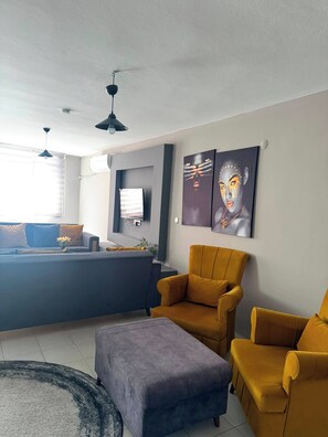A modern living room with a sofa, ottoman, and two armchairs, a flat-screen TV mounted on the wall, and artwork above the seating area. - 2-Bedroom Apartment in Central Pendik, Turkey (Pendik)