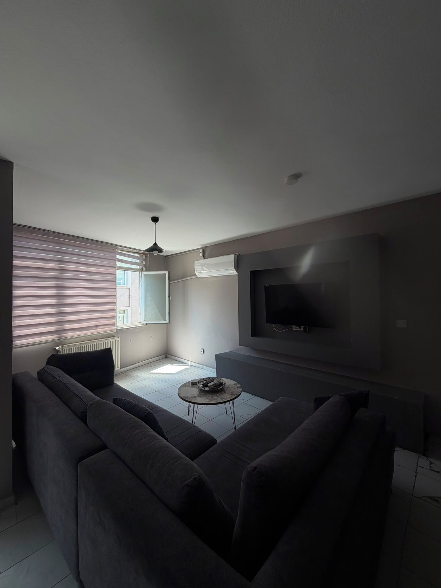 A modern living room with a large gray sofa, a flat-screen TV mounted on the wall, and a ceiling fan.