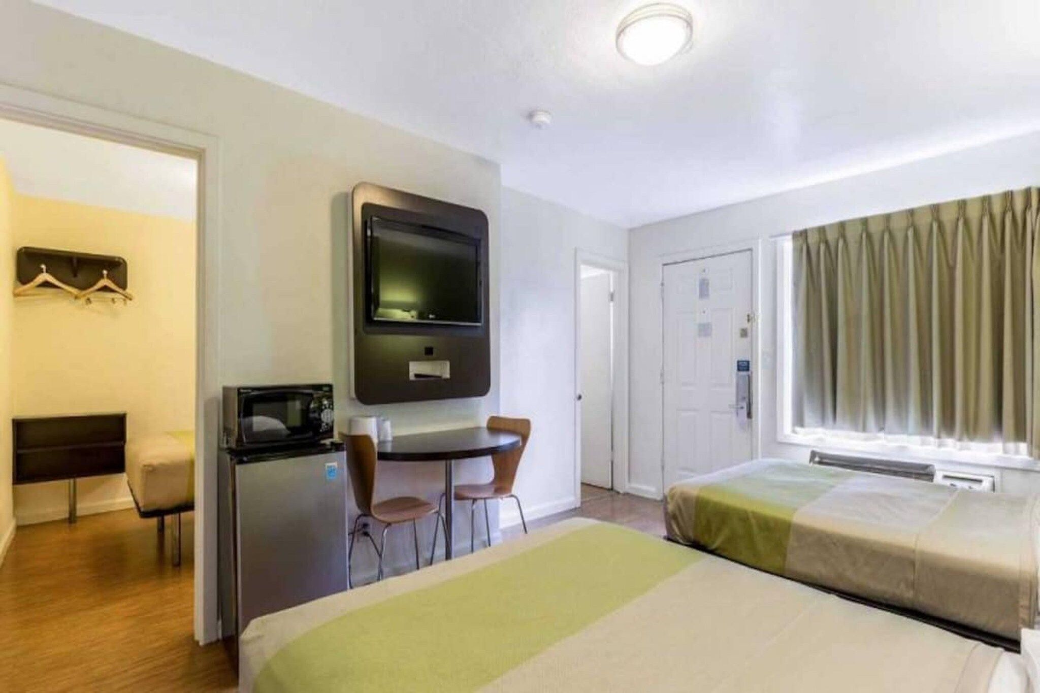 A hotel room with a bed, a desk with a chair, a television, a microwave, and a wardrobe.