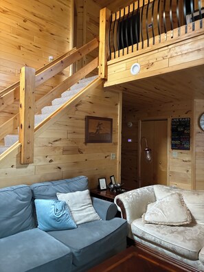 Un interior de madera con una escalera, un sofá y una puerta con un letrero.