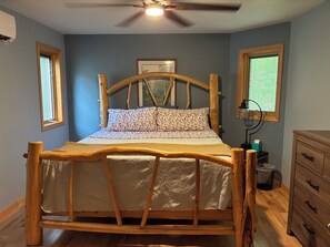Uma cama de madeira com cabeceira, uma mesa de cabeceira com luminária e uma janela com persianas.