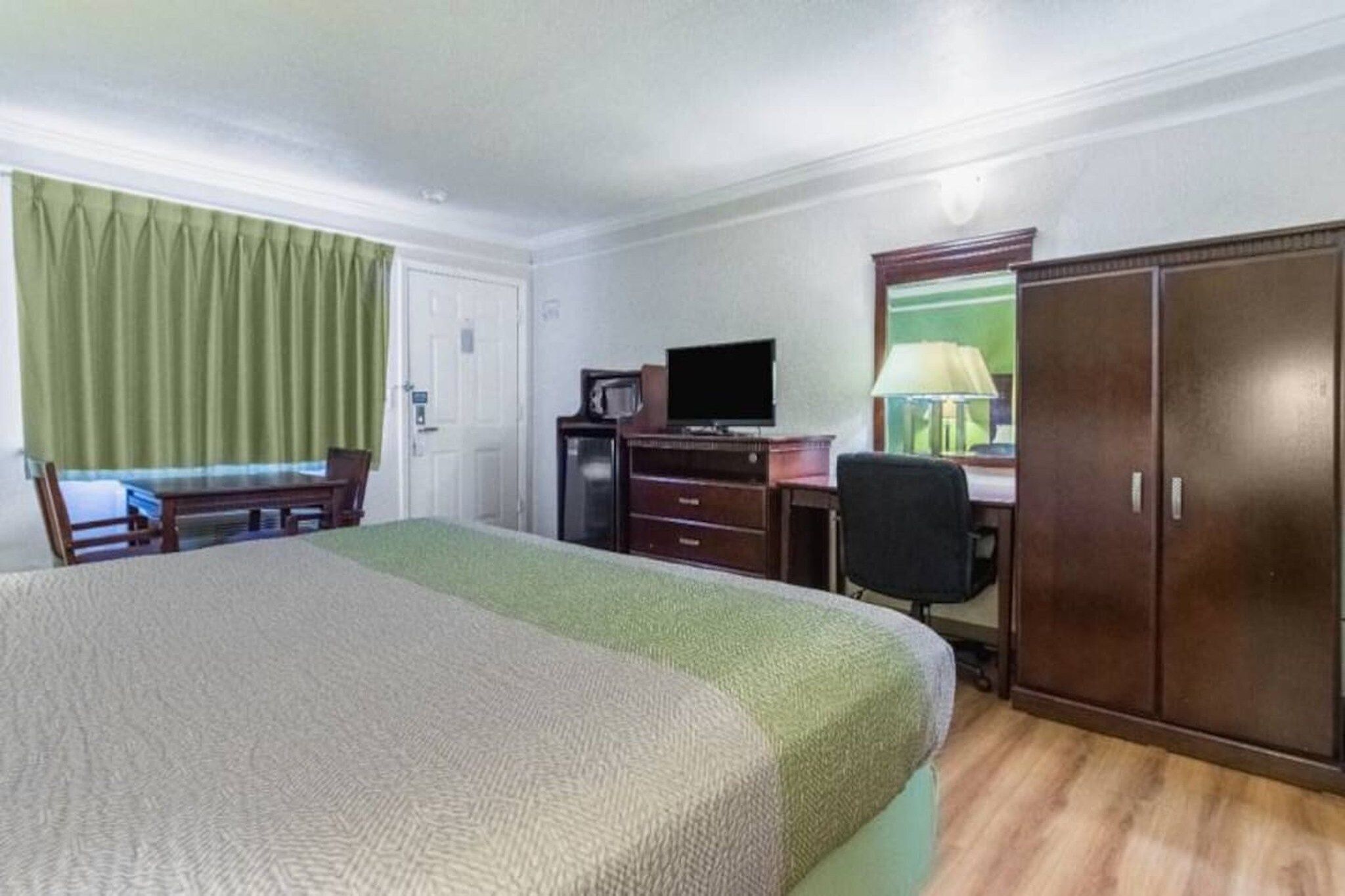 Een hotelkamer met een bed, een bureau, een stoel, een televisie en een kledingkast.