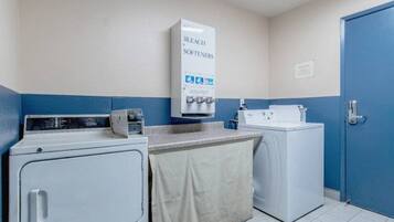 A laundry area with a washing machine, a dryer, and a wall-mounted softener dispenser.