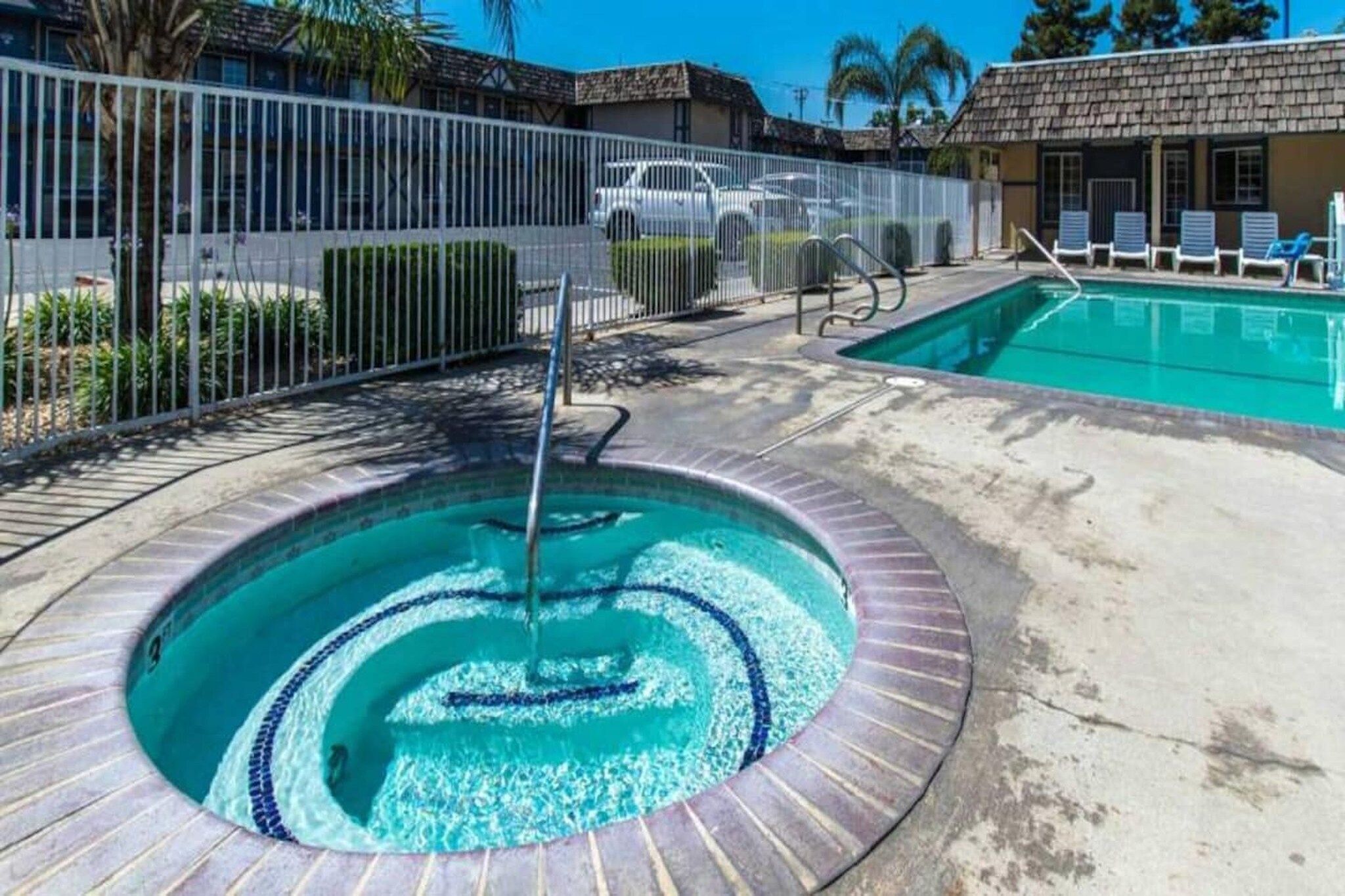 A swimming pool with a circular design, a water fountain, and a fenced area with lounge chairs.