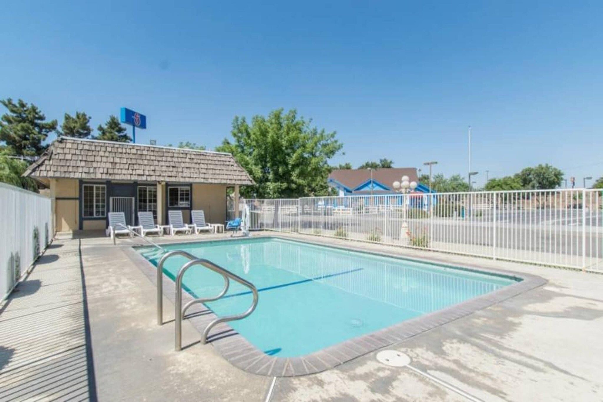 A swimming pool with a fenced area, a small building with a sloped roof, and a clear blue sky.