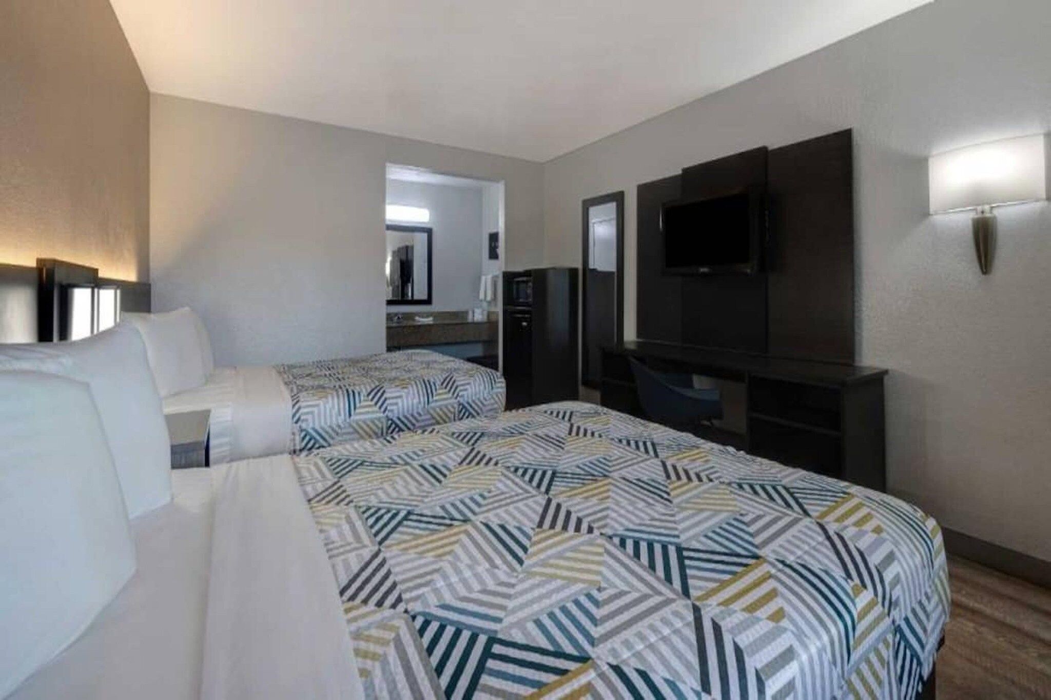 Habitación de hotel con dos camas, un televisor de pantalla plana, minibar y espejo.