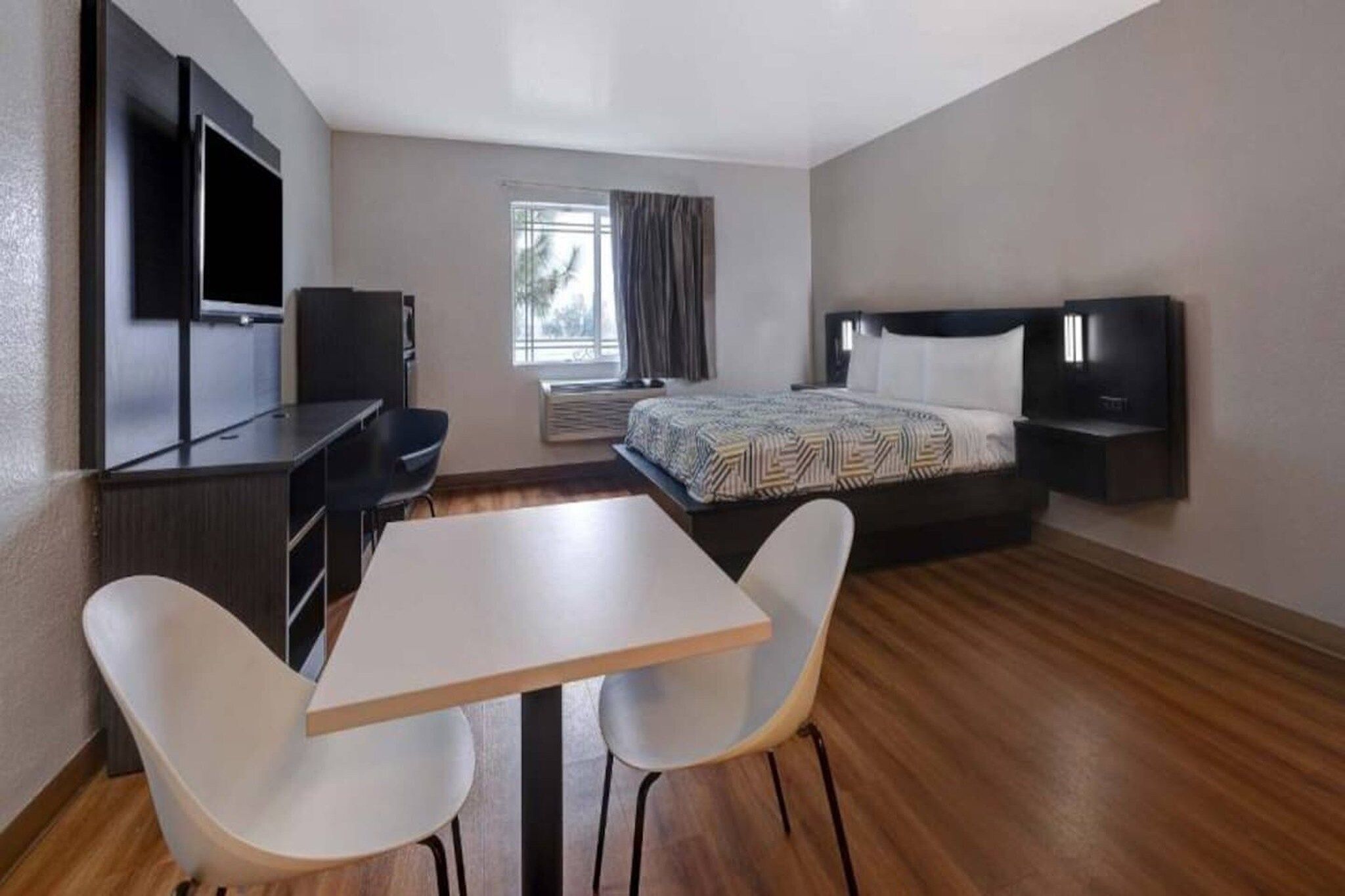 A hotel room with a bed, a TV, a desk, and two chairs.