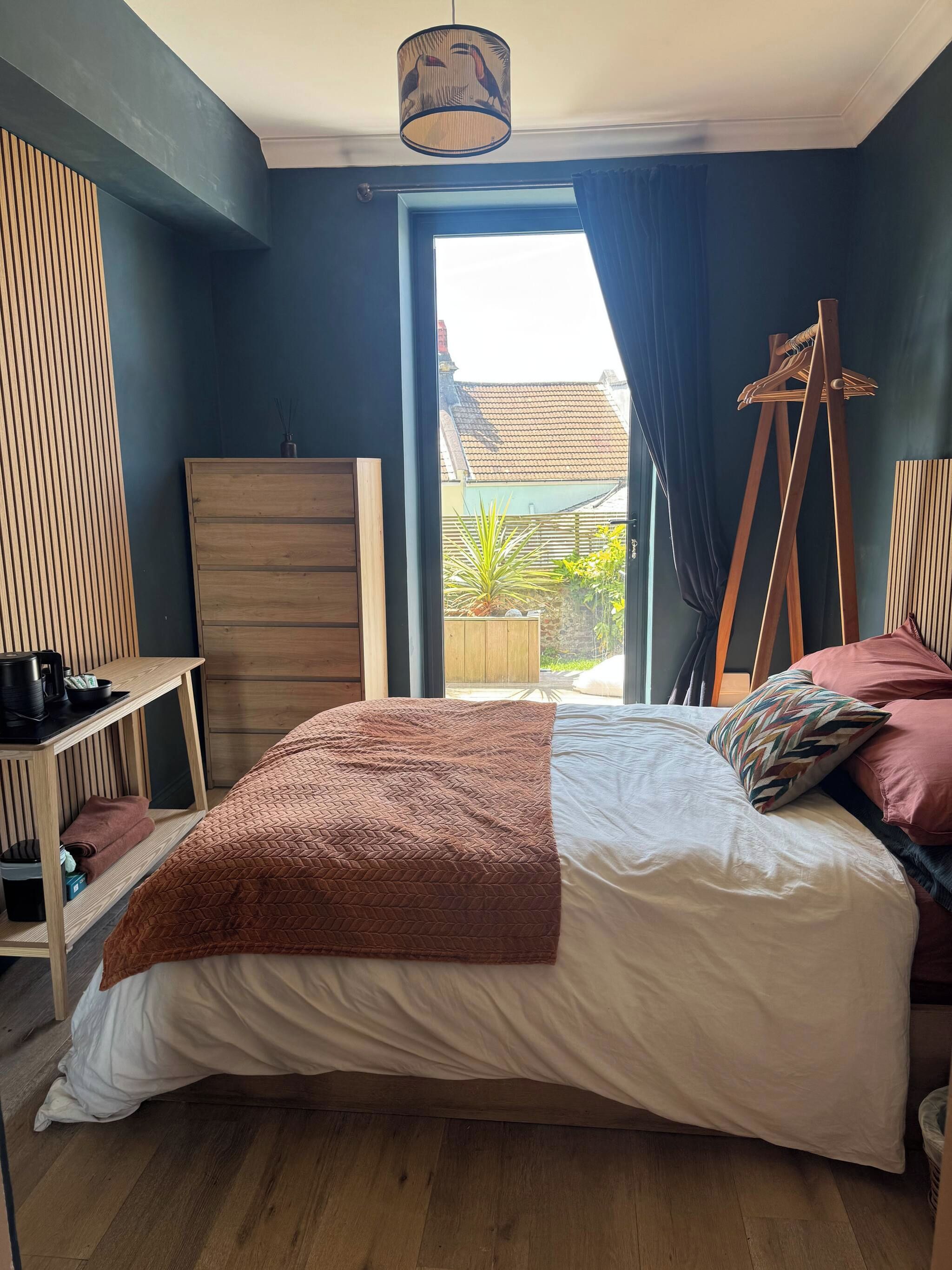 A bedroom with a bed, a wooden dresser, a hanging chair, and a view of the outside.