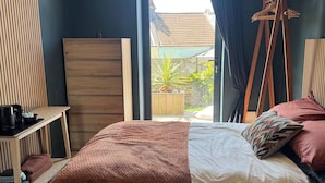 Ein Schlafzimmer mit einem Bett, einer hölzernen Kommode, einem Hängekorbsessel und Blick ins Freie.
