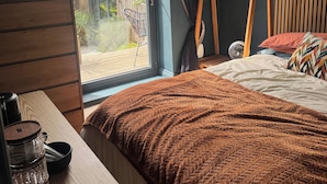 Ein Schlafzimmer mit einem Bett, einer Holzkommode, einem Fenster mit Vorhängen und Blick ins Freie.