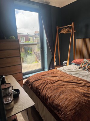 Un dormitorio con cama, cómoda de madera, ventana con cortinas y vista al exterior.