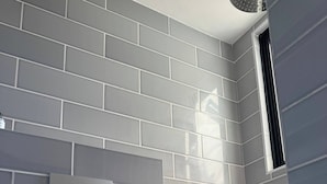 Ein Badezimmer mit grauen Fliesenwänden, einer weißen Toilette und einem Fenster.