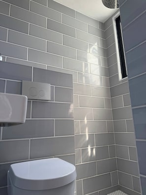 Un baño con paredes de azulejos grises, un inodoro blanco y una ventana.