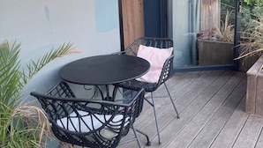 Eine Terrasse mit rundem Tisch, zwei Stühlen, einer Glastür und einem Holzboden.
