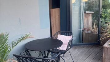A patio with a round table and two chairs, a glass door, and a wooden deck.