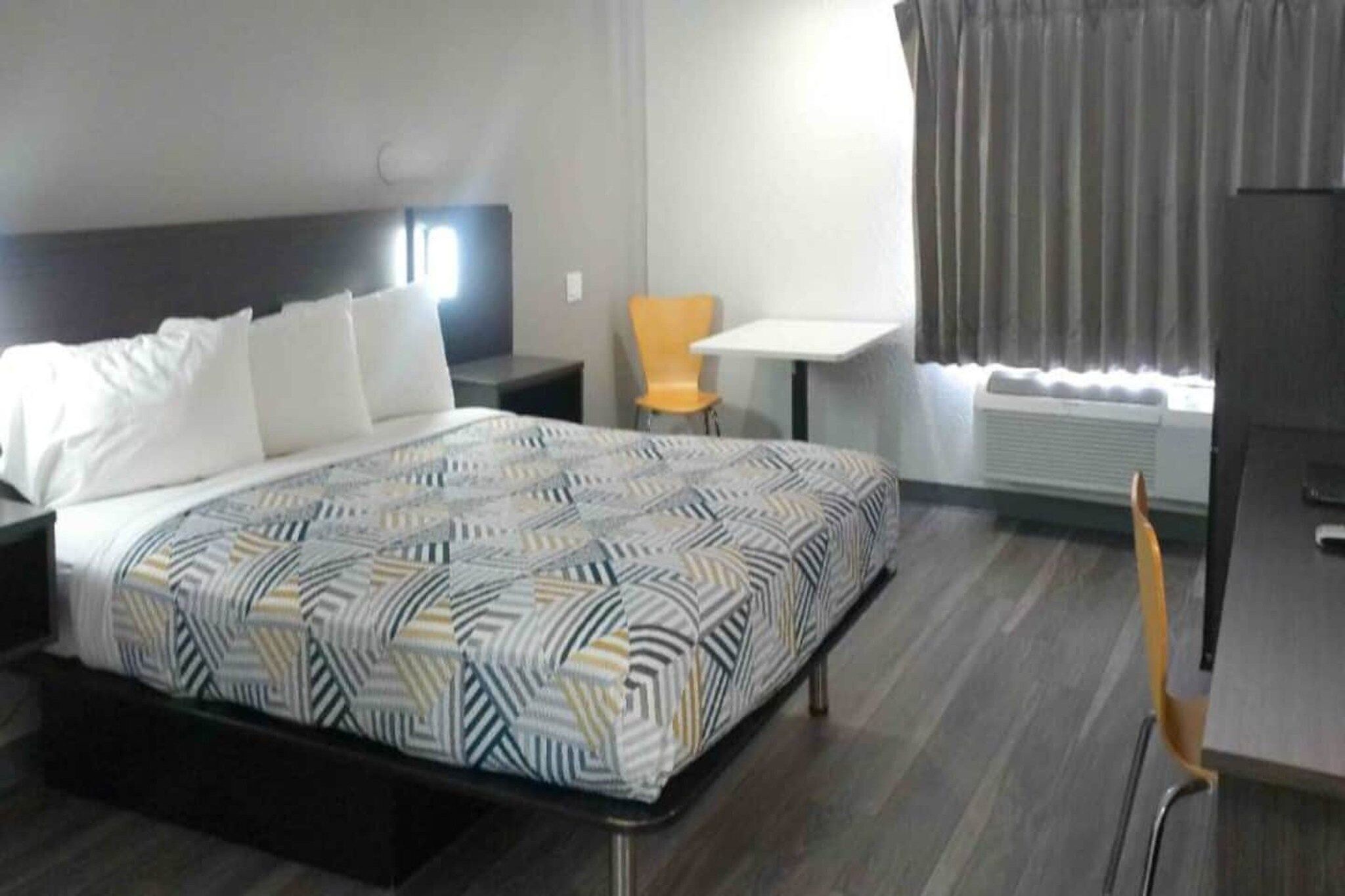Ein Hotelzimmer mit Bett, Sessel, kleinem Tisch und einem Fenster mit Vorhängen.