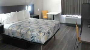 Quarto de hotel com cama, uma cadeira, uma mesa pequena e janela com cortinas.
