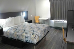 Ein Hotelzimmer mit Bett, Sessel, kleinem Tisch und einem Fenster mit Vorhängen.