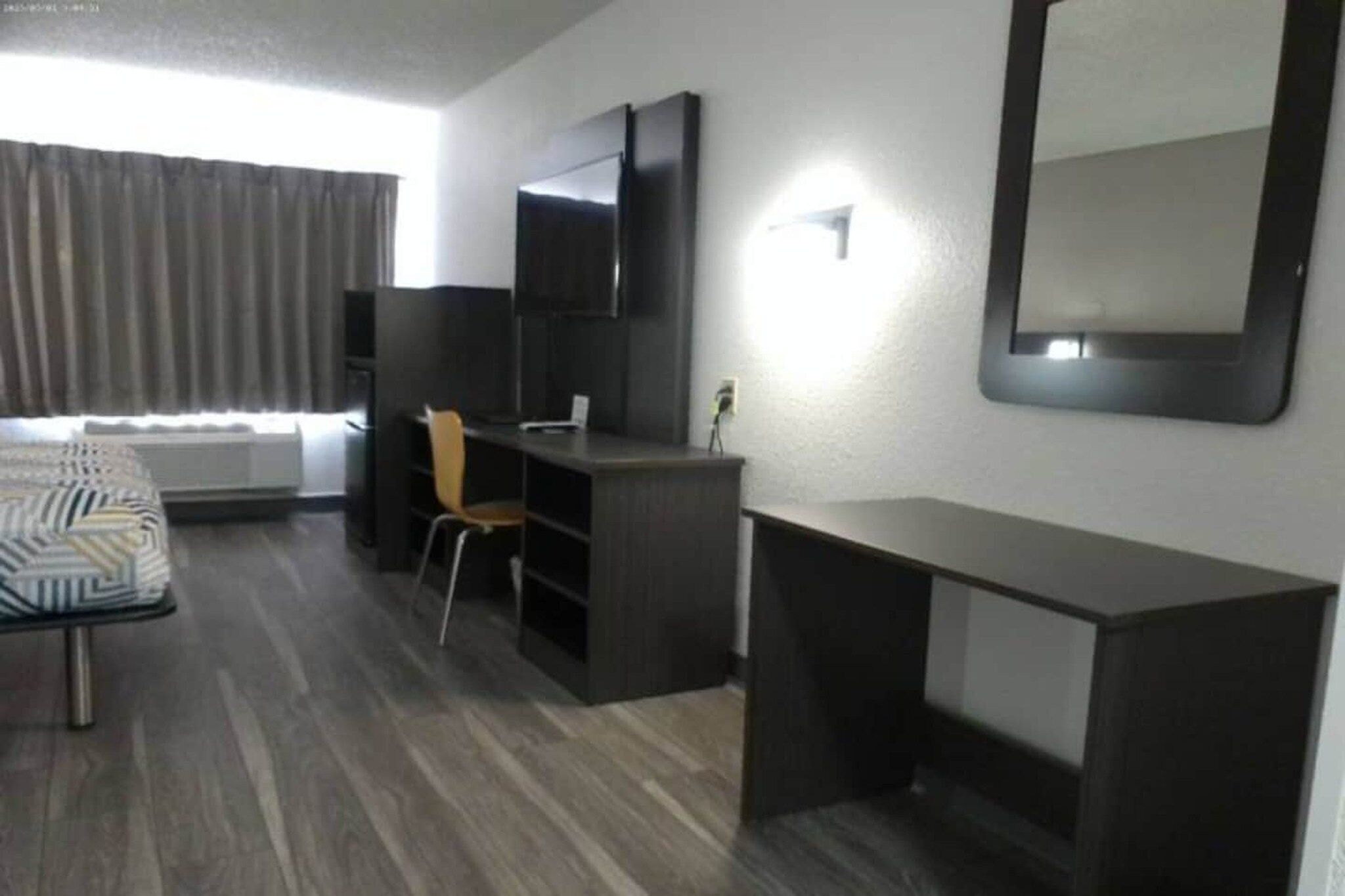A hotel room with a bed, a desk, a chair, a wardrobe, and a large mirror on the wall.