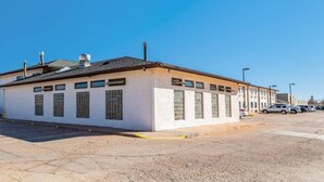 Um edifício térreo com telhado plano, grandes janelas e um estacionamento em frente.