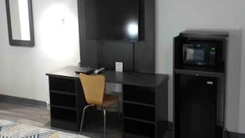 A room with a desk, chair, television, and a microwave.