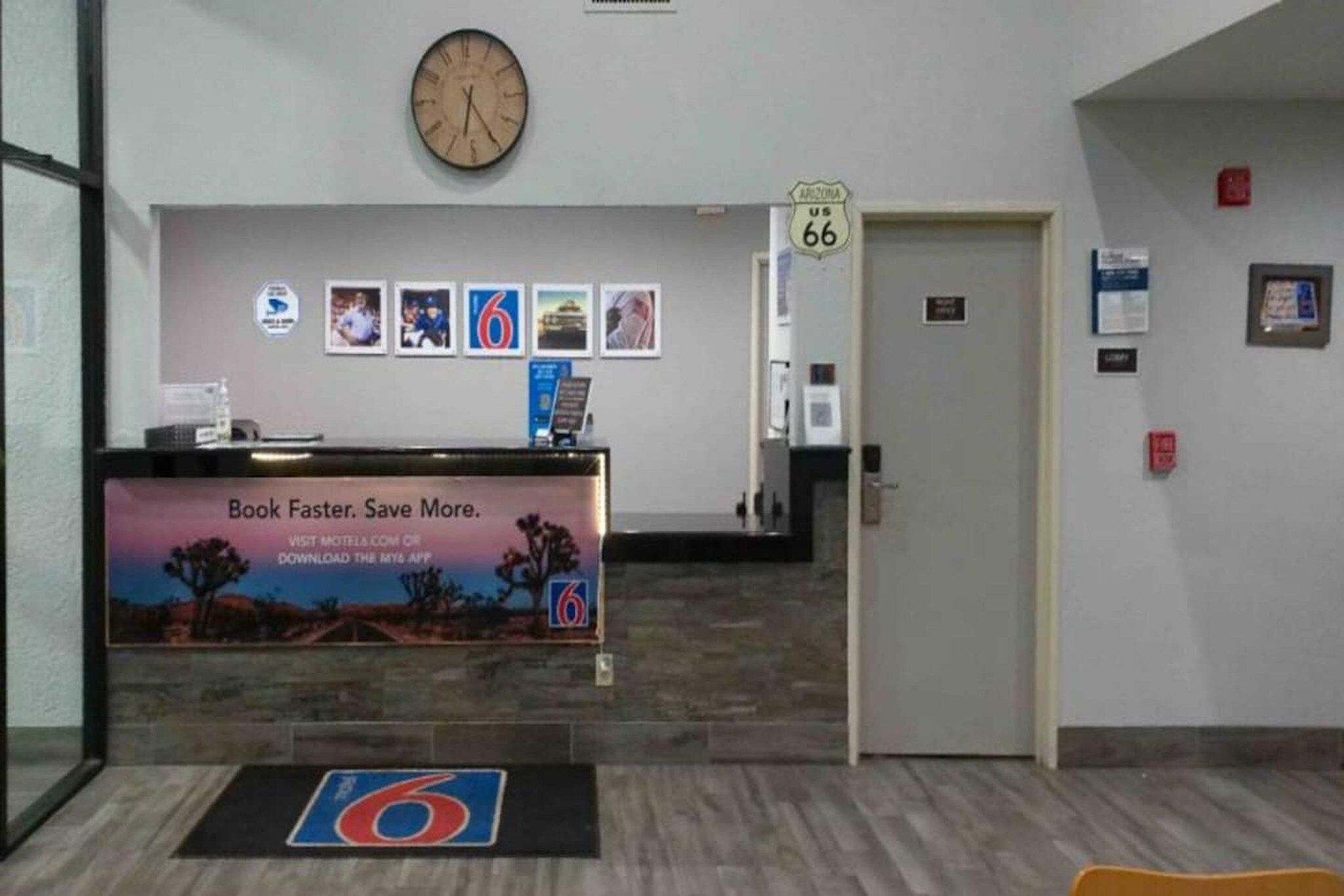 A reception area with a clock, framed pictures, a sign for room number 66, and a promotional poster for a mobile app.