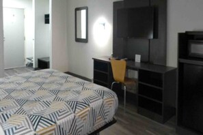 A hotel room with a bed, a desk, a chair, a TV, and a wardrobe.