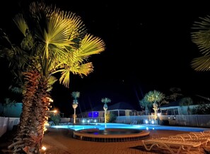 Un espace piscine aménagé pour la nuit, avec des palmiers et un jacuzzi.