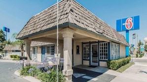 A motel with a single-story structure, a covered entrance, and a clear blue sky in the background. - Premium King Bed|Pool|Free Parking (Kingsburg)
