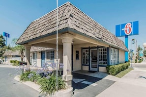 Un motel con una estructura de un solo piso, un acceso cubierto y un cielo azul despejado al fondo.