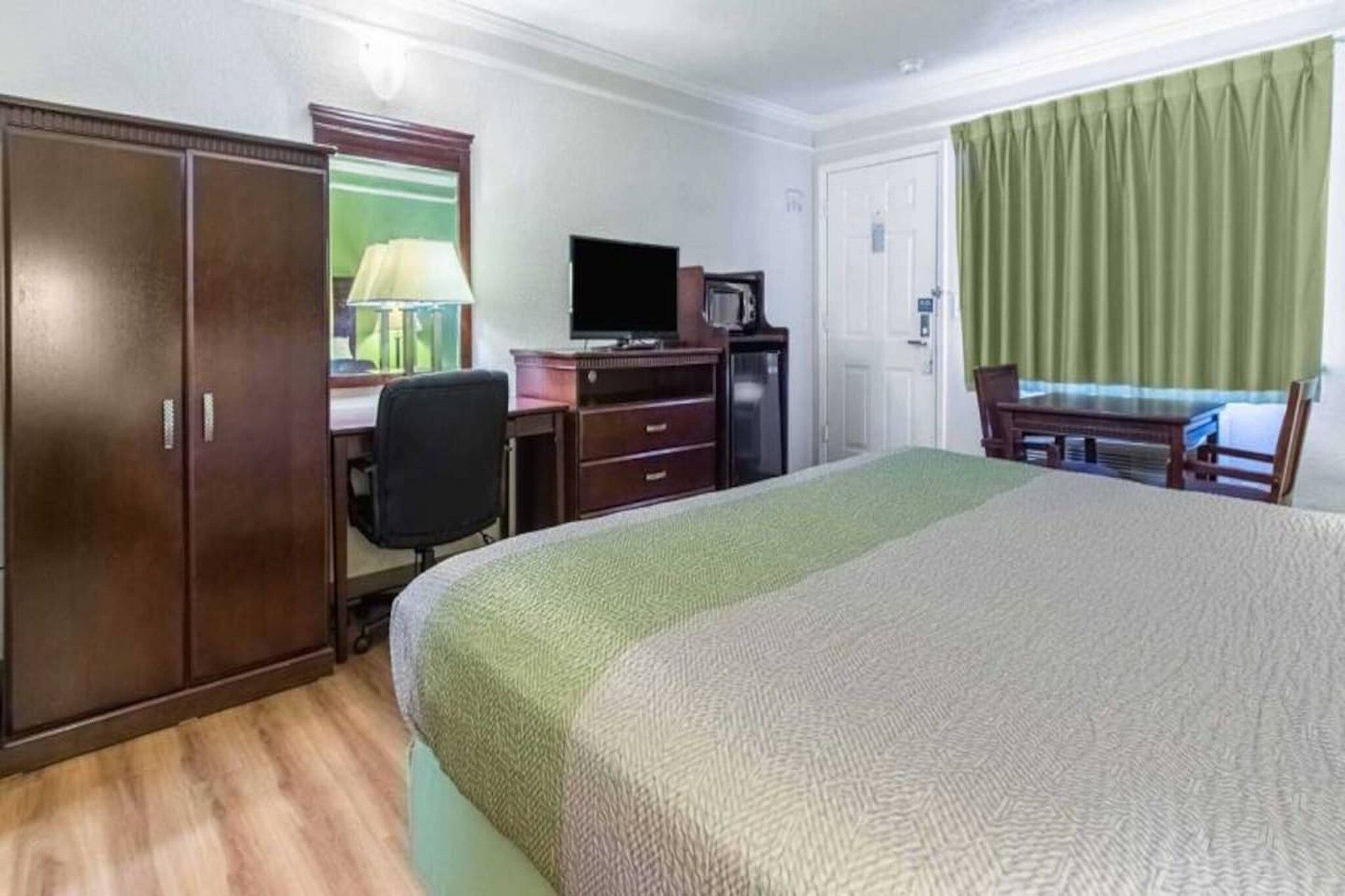 Een hotelkamer met een bed, een bureau met stoel, een televisie en een kledingkast.