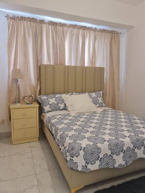 Une chambre à coucher avec un lit, une table de chevet, une lampe et une fenêtre avec des rideaux.