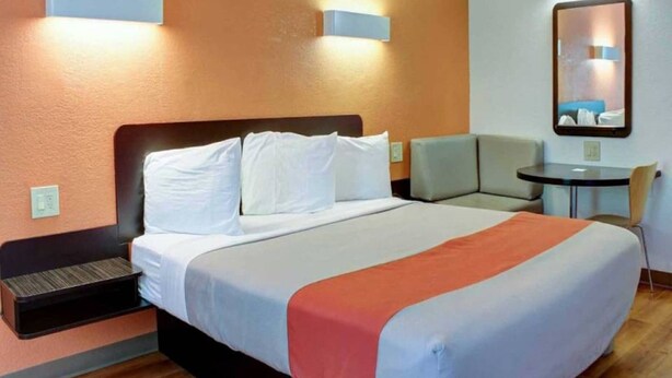 Quarto de hotel com cama, mesas de cabeceira, uma cadeira, uma mesinha e um espelho na parede.