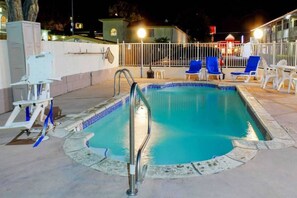 Ein Swimmingpool mit einer Metallleiter, umgeben von einem weißen Zaun und blauen Liegestühlen.