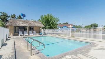 A swimming pool with a fenced area, a small building with a sloped roof, and a clear blue sky.