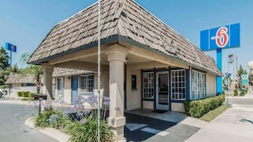 Un motel con una estructura de un solo piso, un acceso cubierto y un cielo azul despejado al fondo.