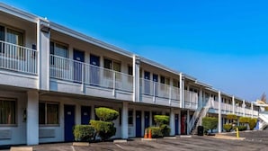 Um motel com uma fileira de quartos, cada um com porta e uma pequena varanda.