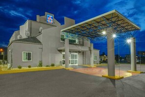 Un hotel con entrada techada, un llamativo letrero con el número '6' y un estacionamiento.