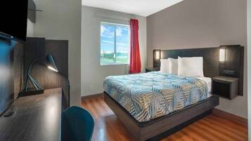 A hotel room with a bed, bedside tables, a desk, a chair, a window with a view, and a red curtain.