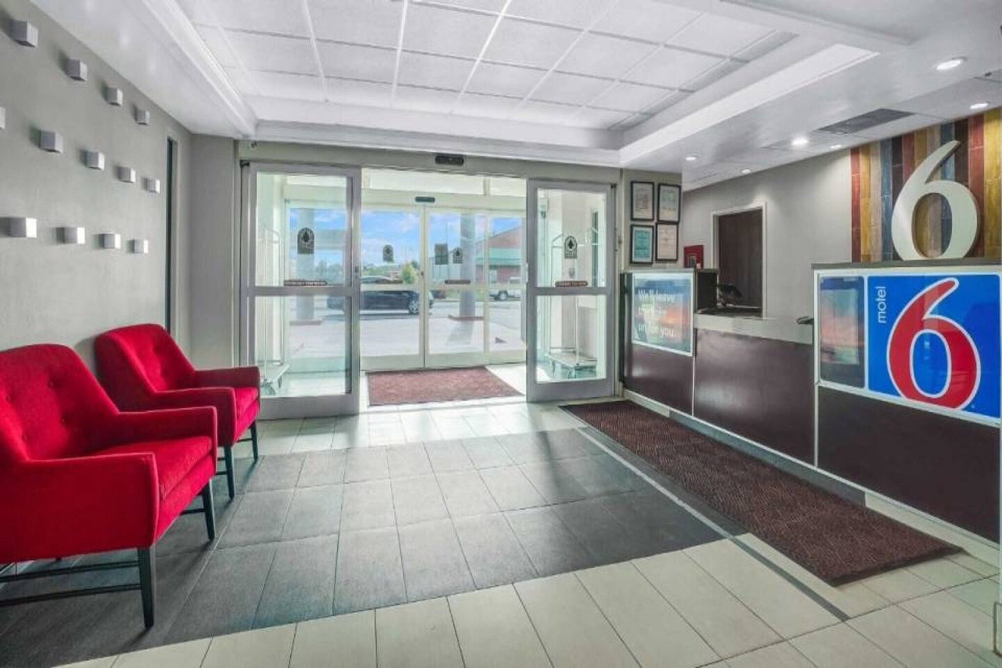 A hotel lobby with a reception desk, a glass door entrance, and red chairs.