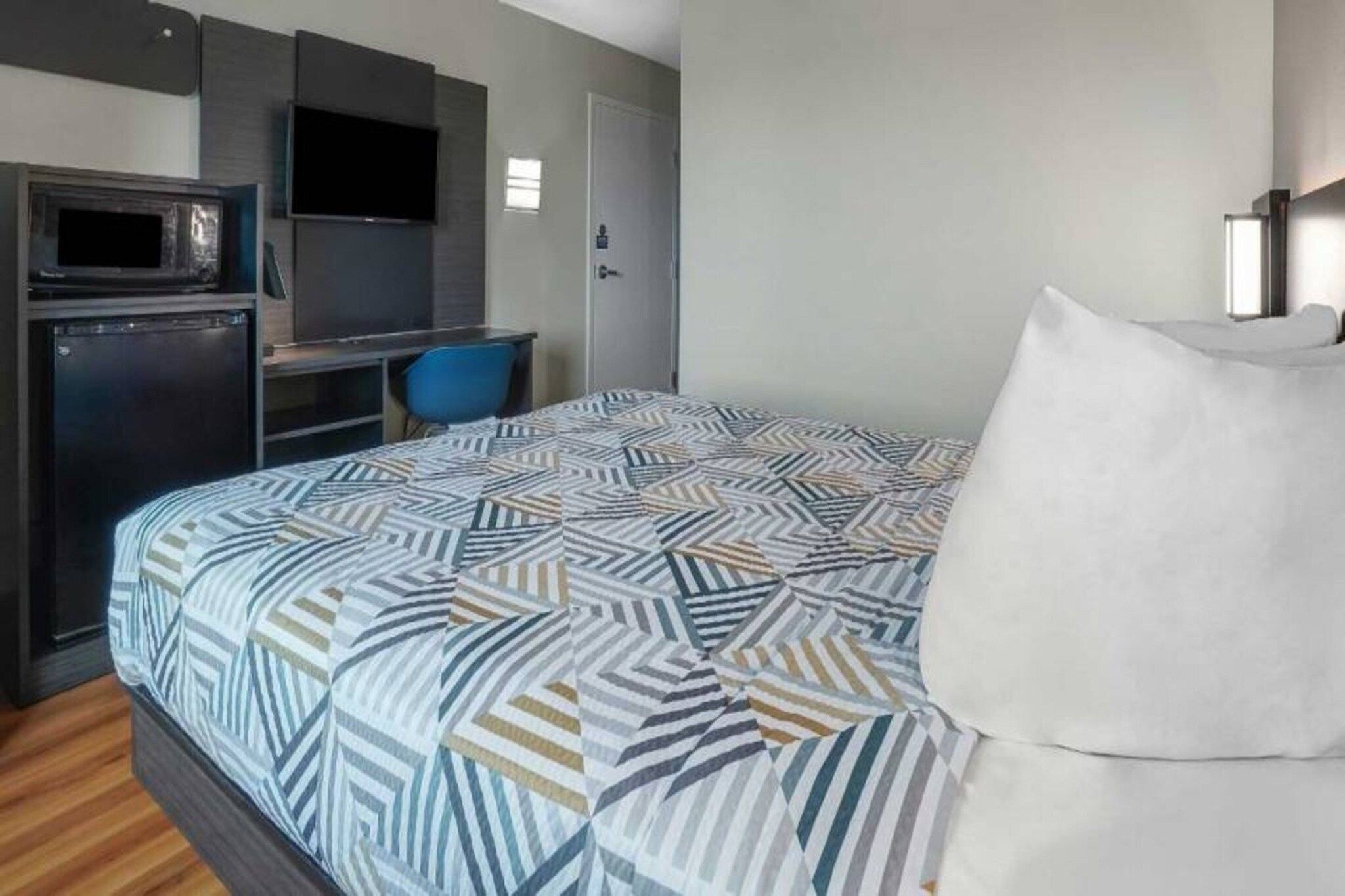 A hotel room with a bed, a desk with a computer, a chair, and a television.