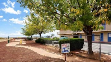 A motel with a sign indicating a pet area, surrounded by trees and a fenced parking lot.
