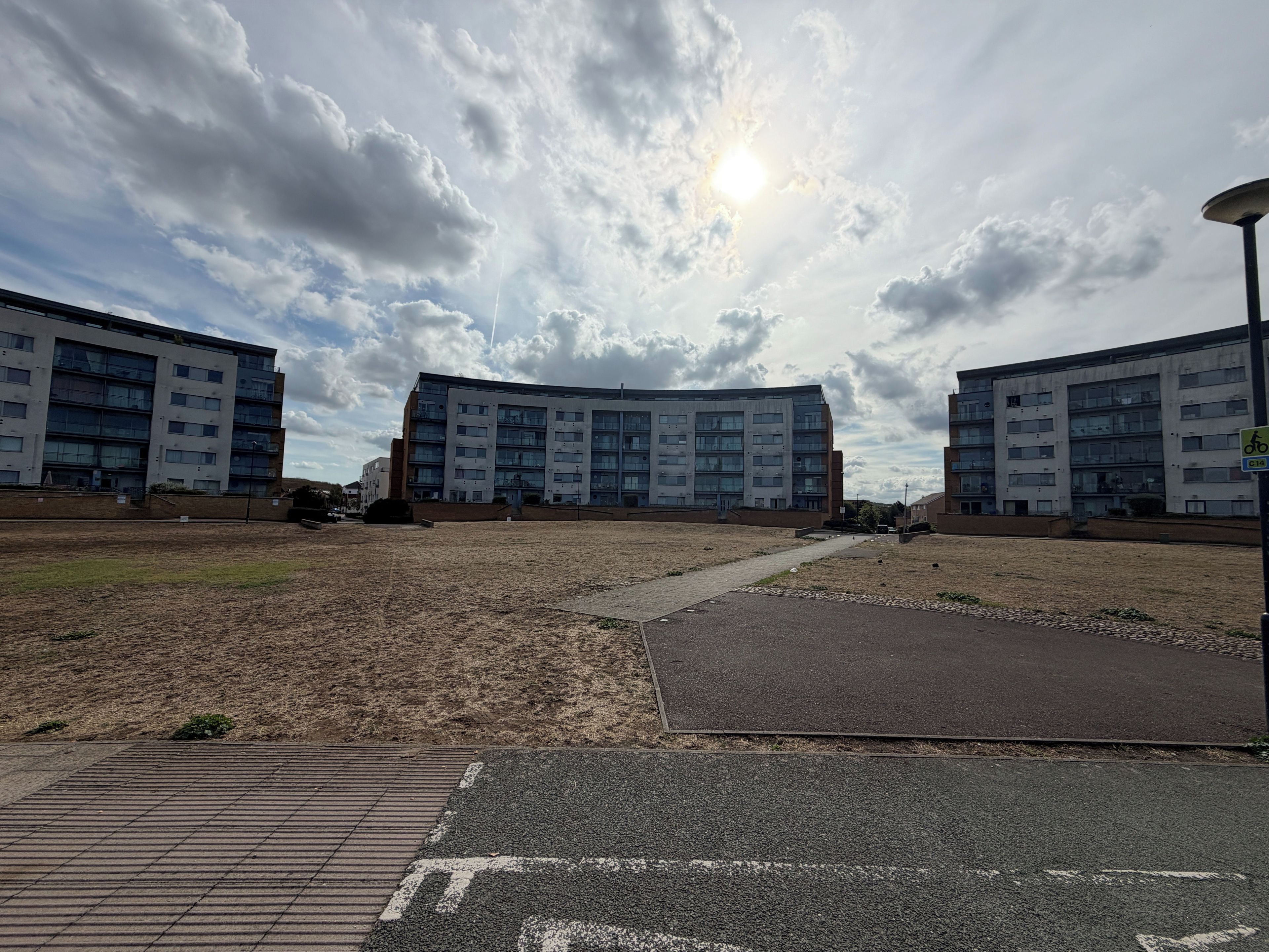 A modern apartment building with multiple floors and balconies, a paved area in front, and a clear sky with clouds.