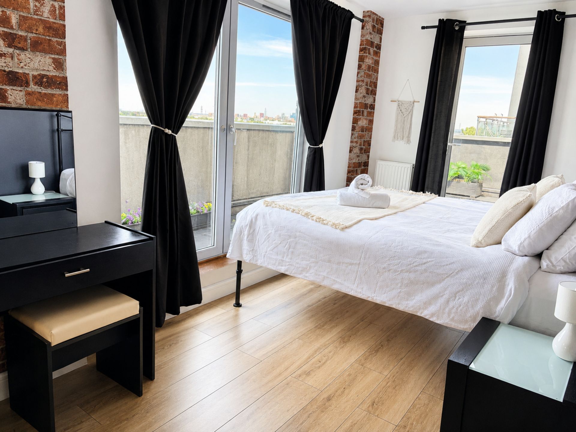 Un dormitorio moderno con cama, escritorio y vistas de la ciudad a través de amplias ventanas.