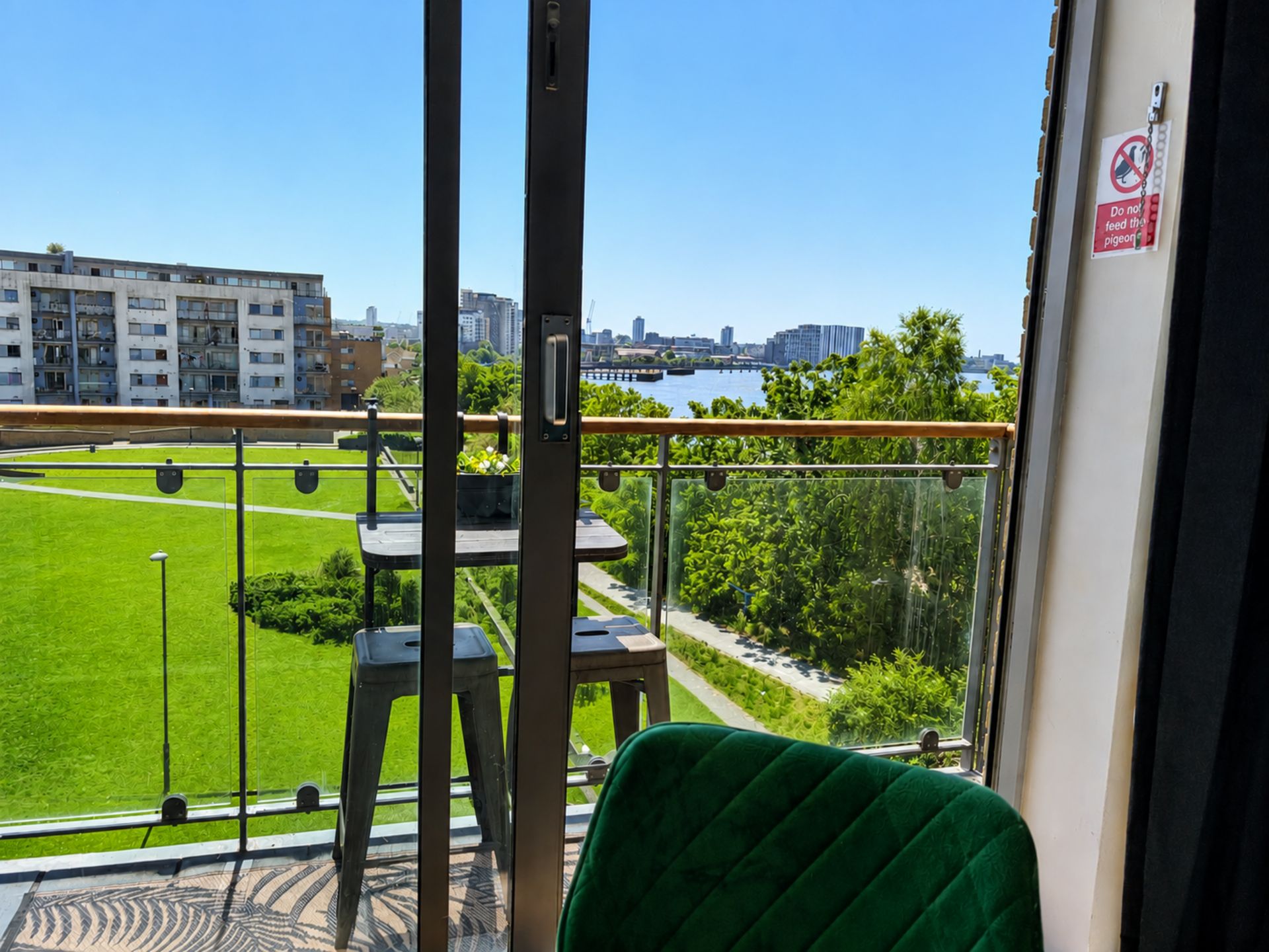 Un balcon offrant une vue sur un terrain de sport verdoyant, le panorama de la ville et une rivière.
