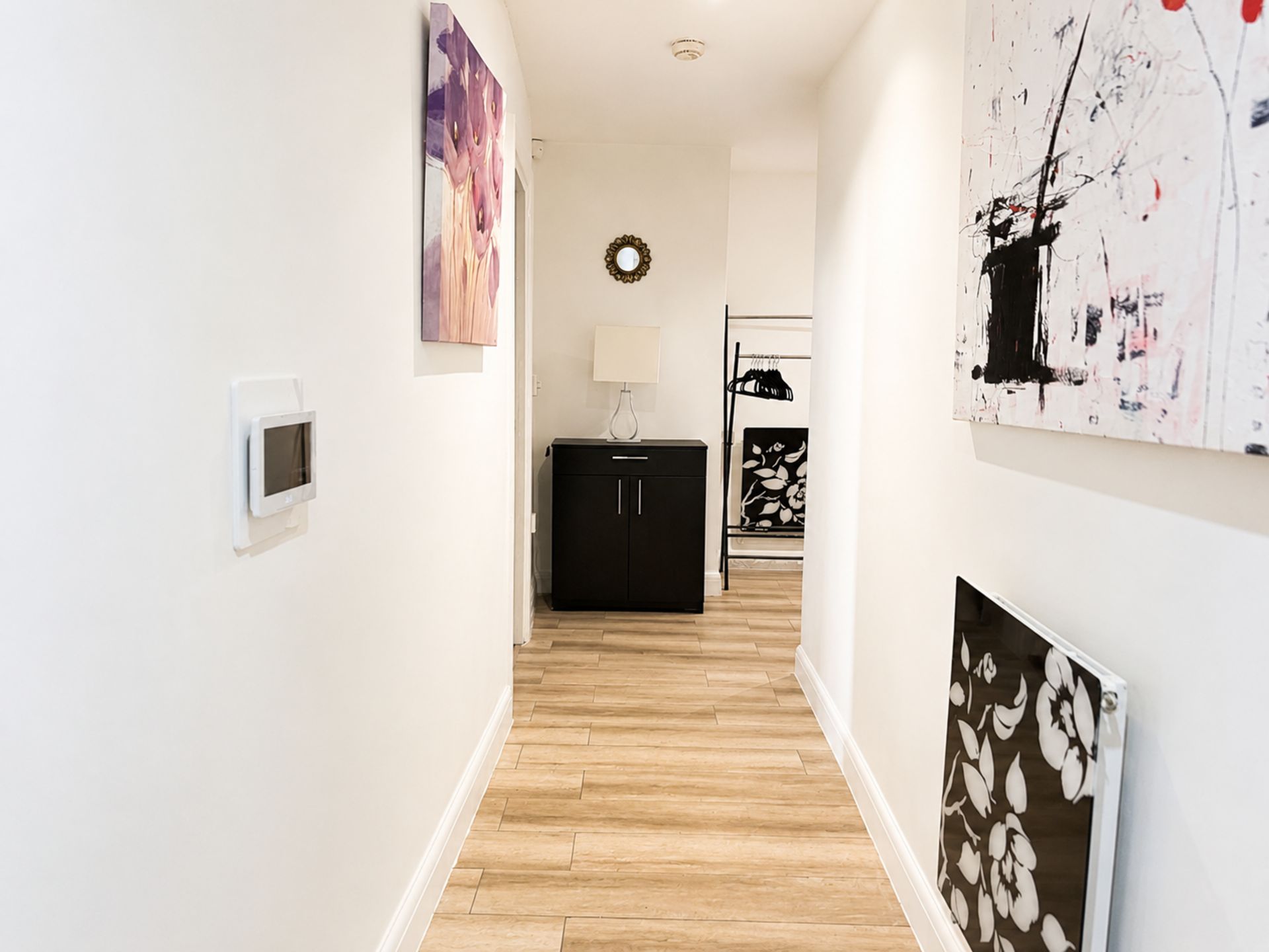 A hallway with a wooden floor, a black cabinet, and artwork on the walls.