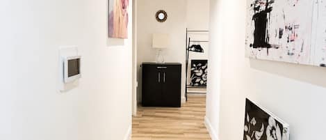 A hallway with a wooden floor, a black cabinet, and artwork on the walls.